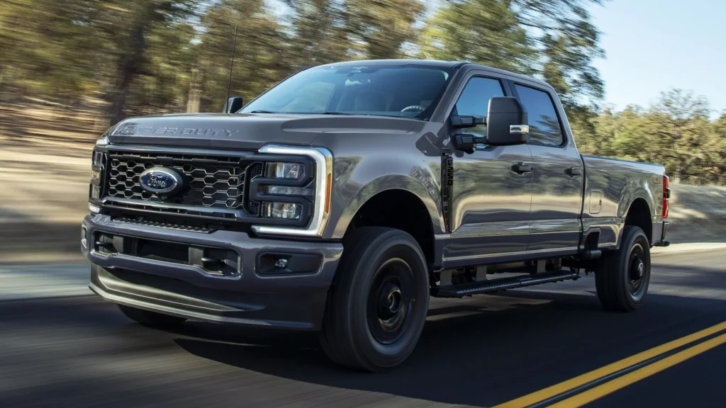 Gray 2025 Ford Super Duty F-250 pickup truck driving on a road lined with trees in daylight.