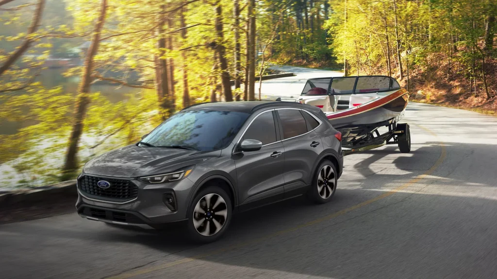 2025 Ford Escape® towing a speedboat along a wooded lakeside road in daylight