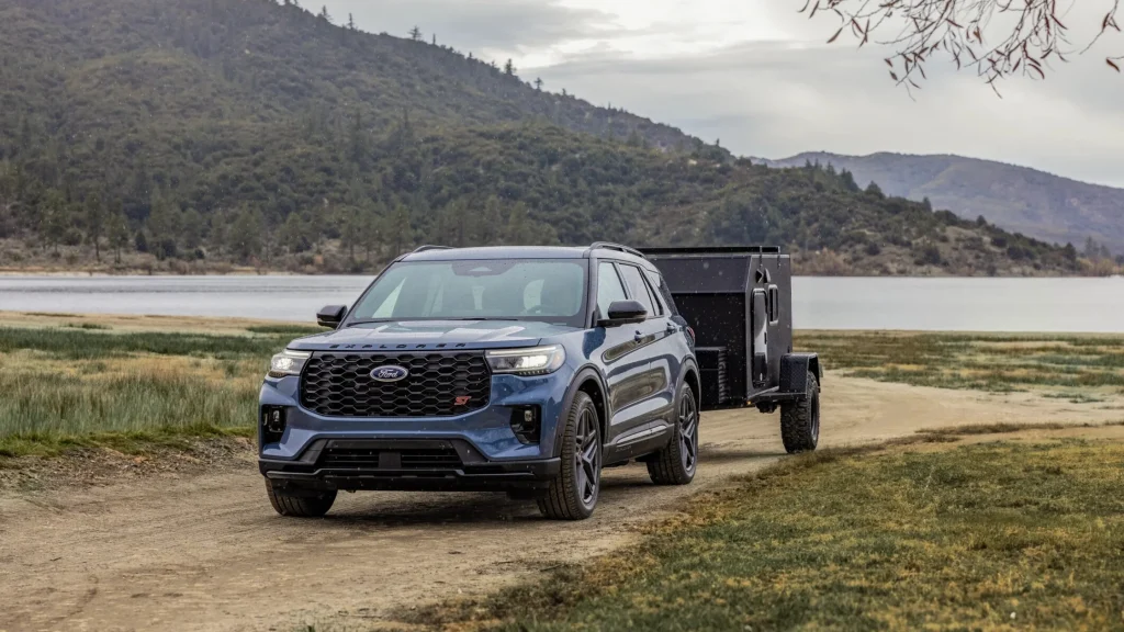 2025 Ford Explorer® ST pulling a utility trailer on a dirt road near a mountain lake