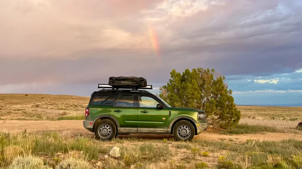 Green 2025 Bronco Sport® Overland parked in desert with rooftop cargo under rainbow sky.