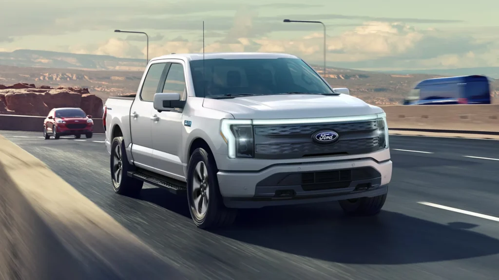 White 2025 F-150® Lightning driving on highway with LED light bar and desert canyon background.
