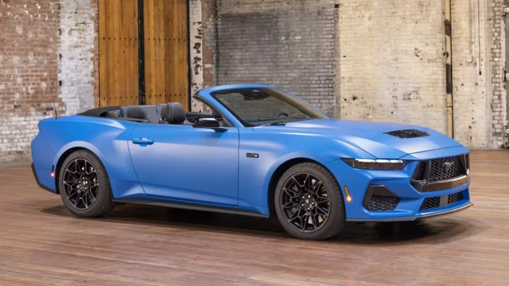 Blue 2025 Mustang® Convertible sports car with black wheels parked in rustic industrial space.