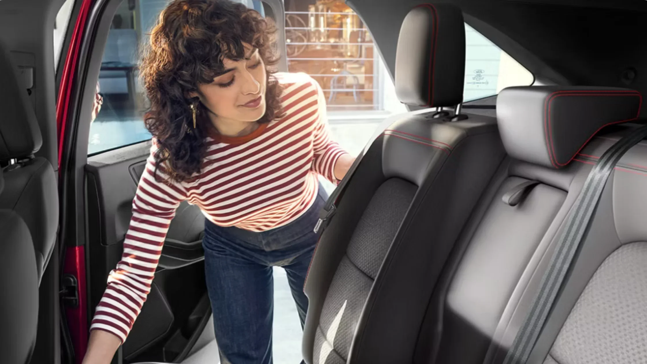 Woman adjusting the rear seat inside the 2025 Ford Escape® ST-Line Hybrid with red-stitched trim.