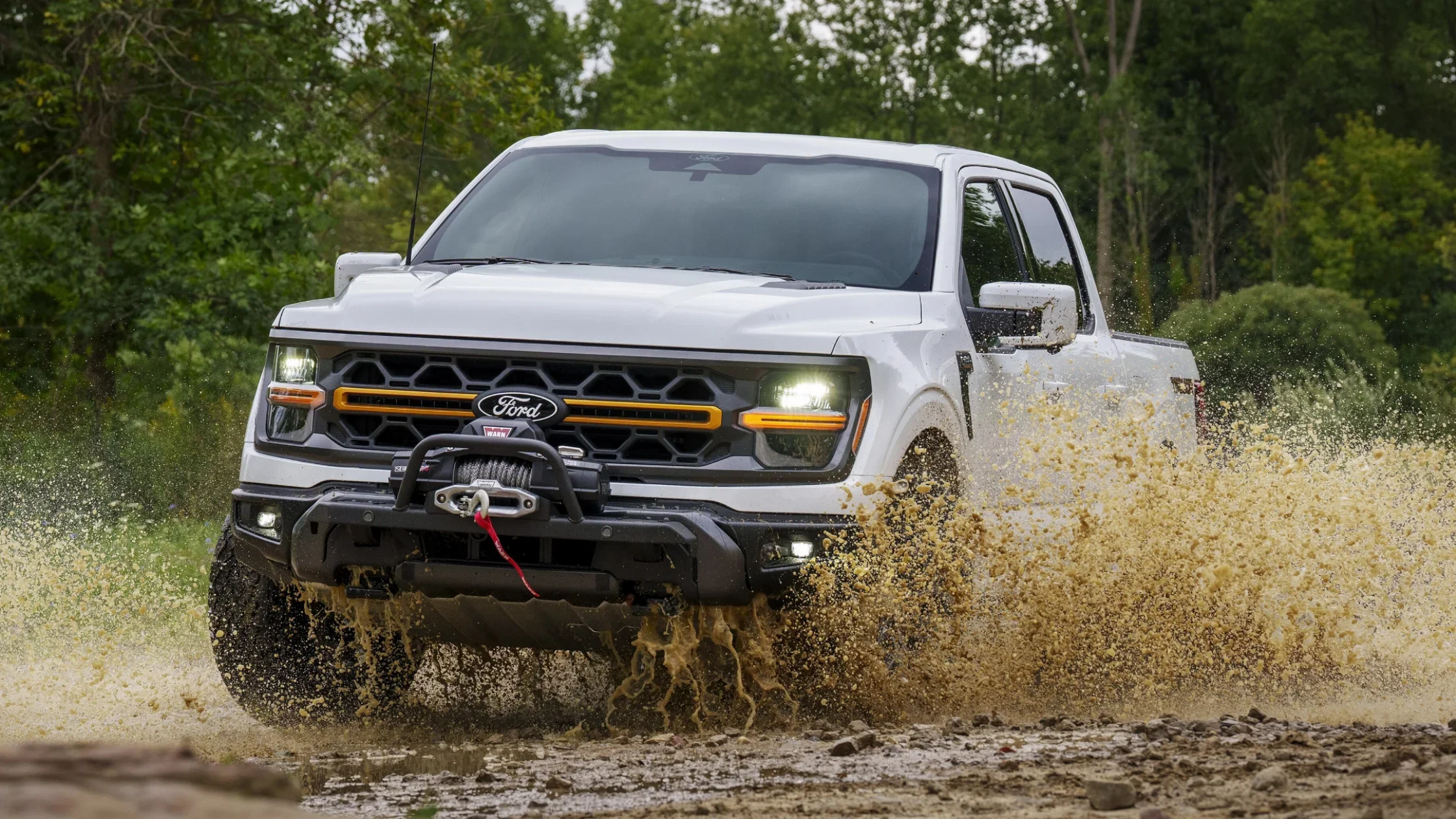White 2025 F-150® pickup truck splashing through mud with off-road winch attached.
