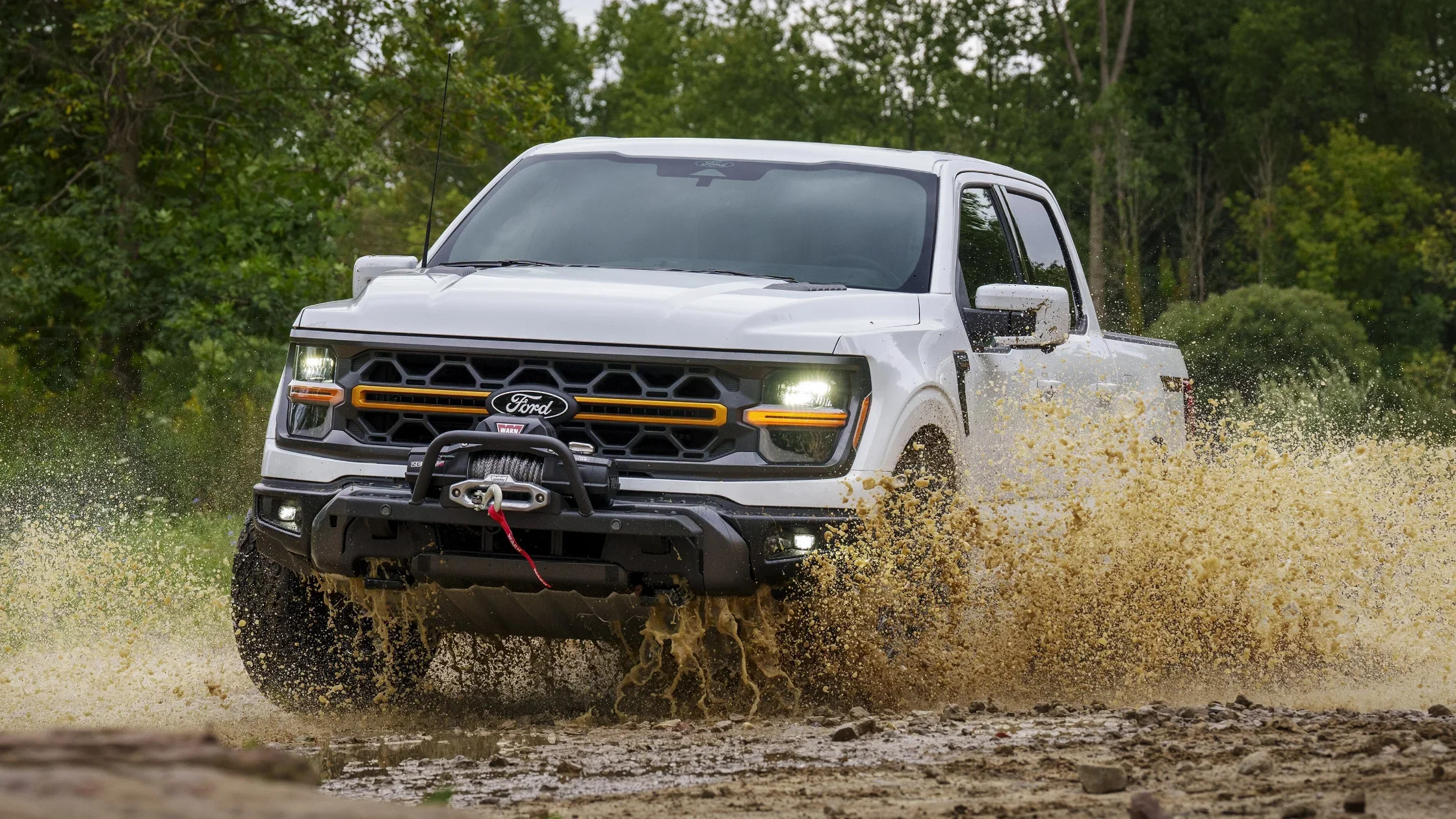 2025 Ford F-150 driving through mud in off-road setting with front winch engaged