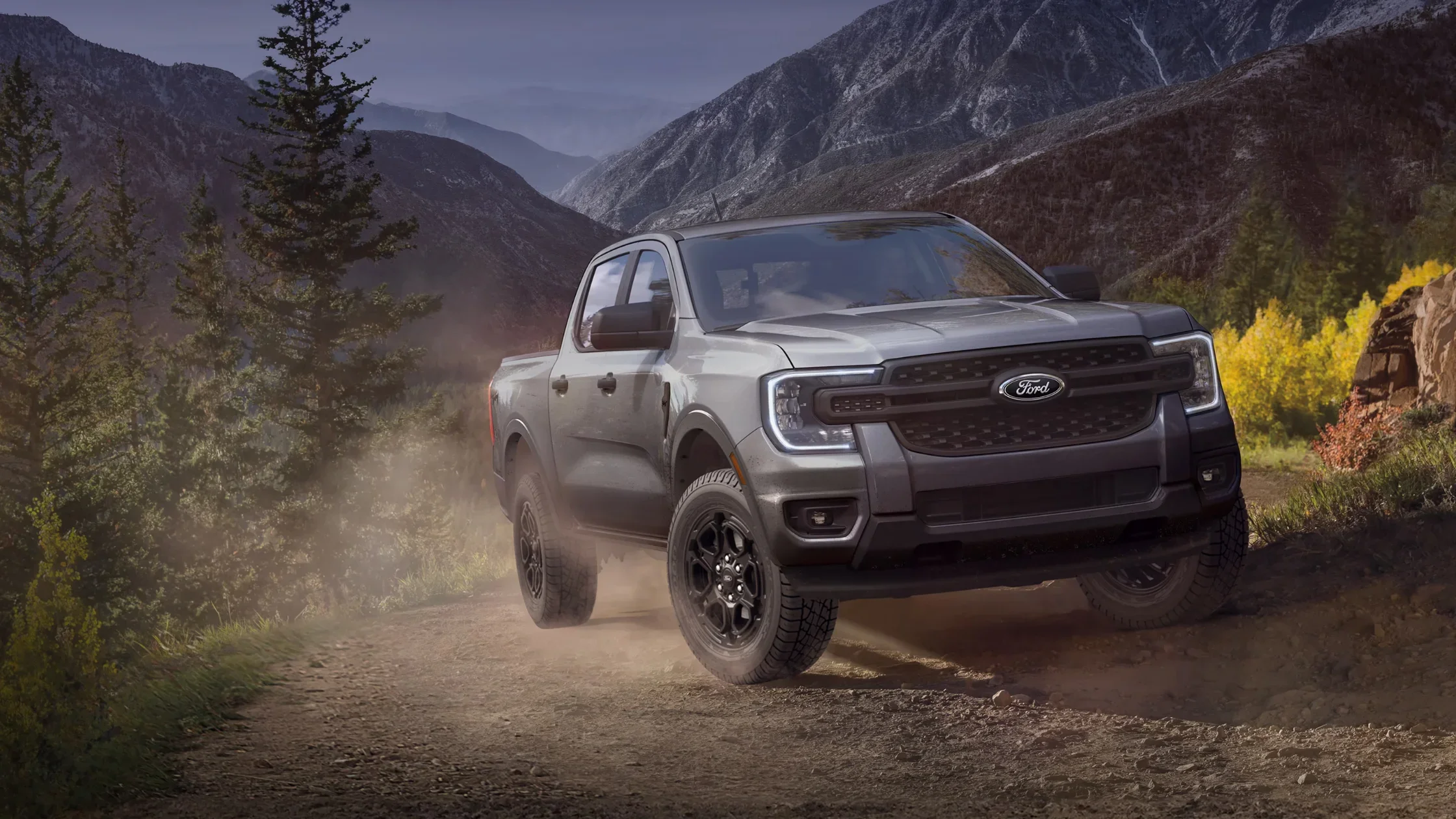 2025 Ford Ranger pickup driving on dusty mountain trail with rugged terrain and forest trees