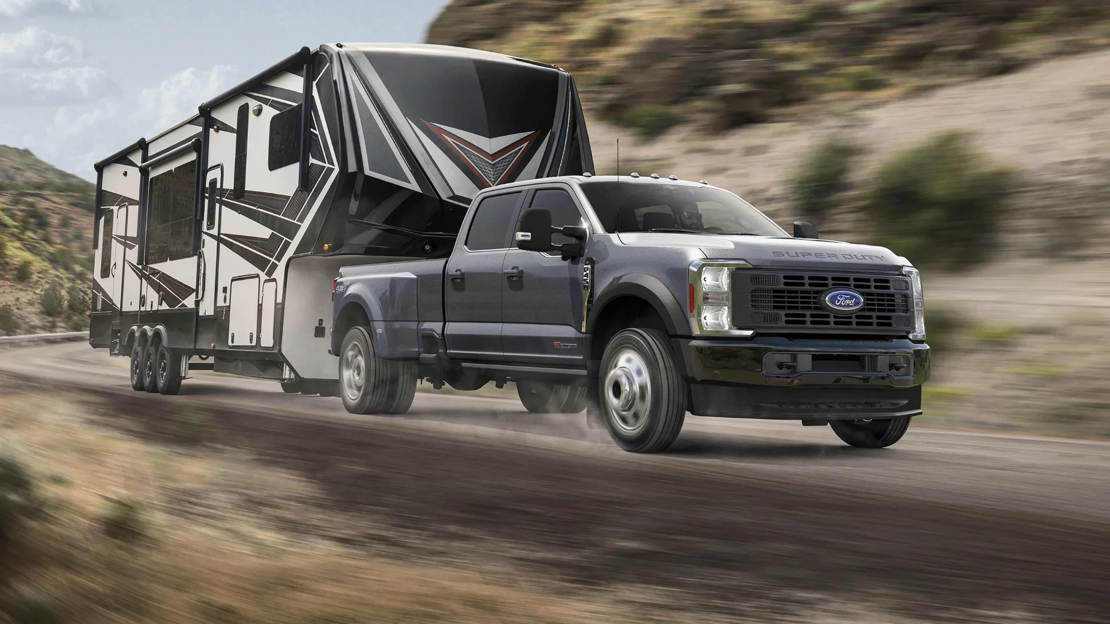 2025 Ford Super Duty towing a fifth-wheel camper on mountain road with rugged terrain