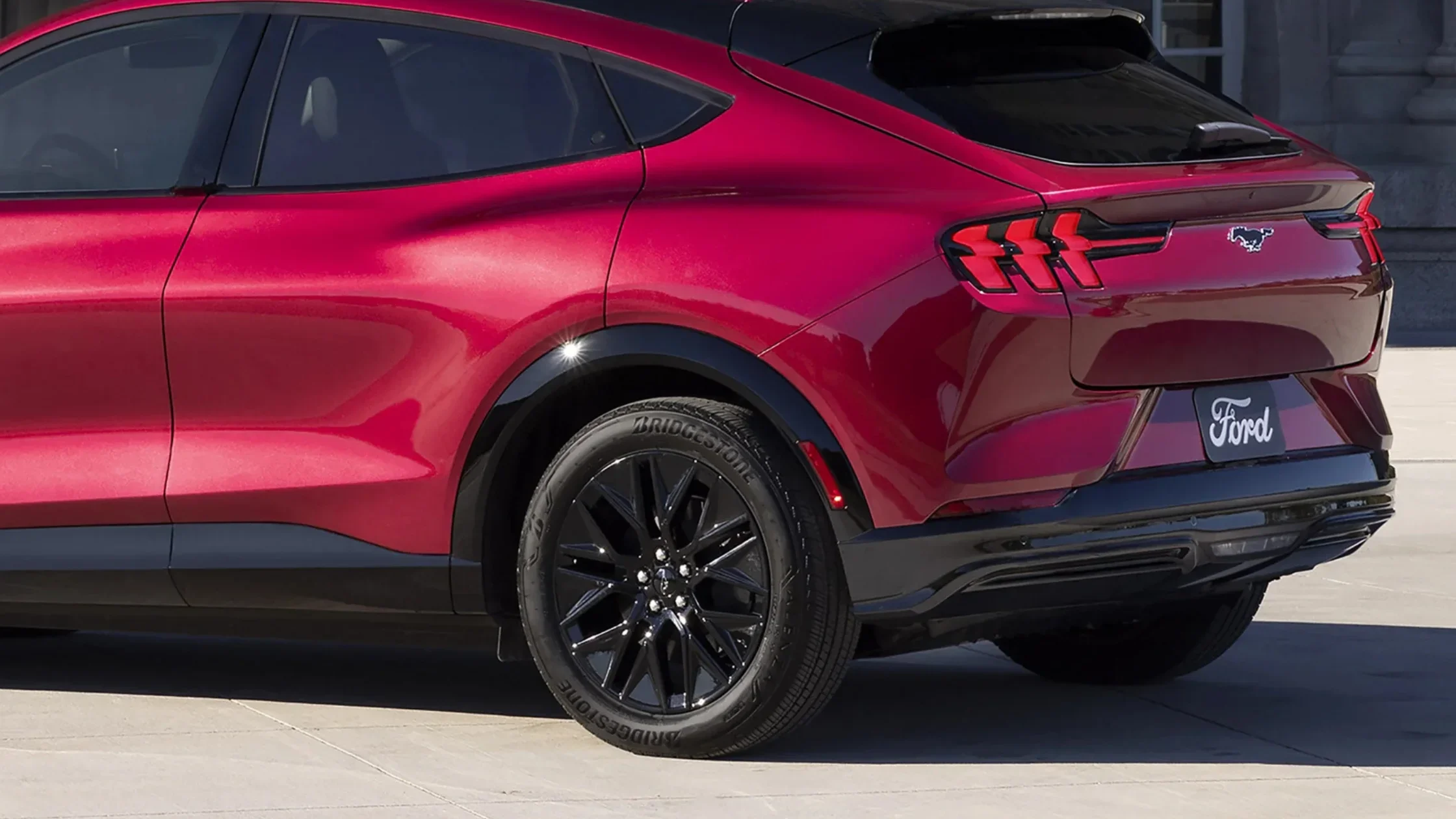 Rear view of 2025 Mustang Mach-E® in red with tri-bar LED taillights and black alloy wheels