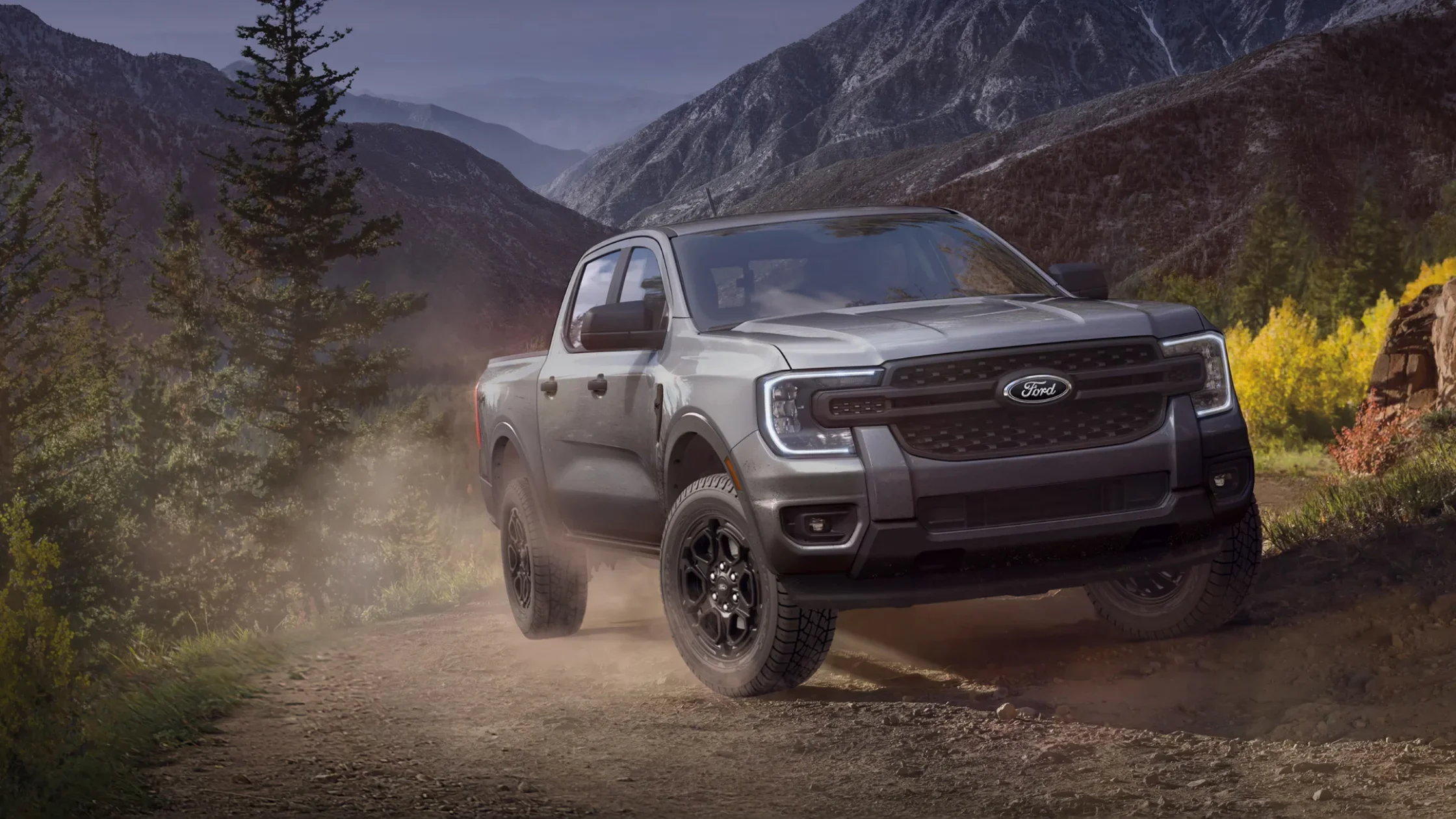 Gray 2025 Ranger® pickup truck driving on dusty mountain trail with rugged terrain.