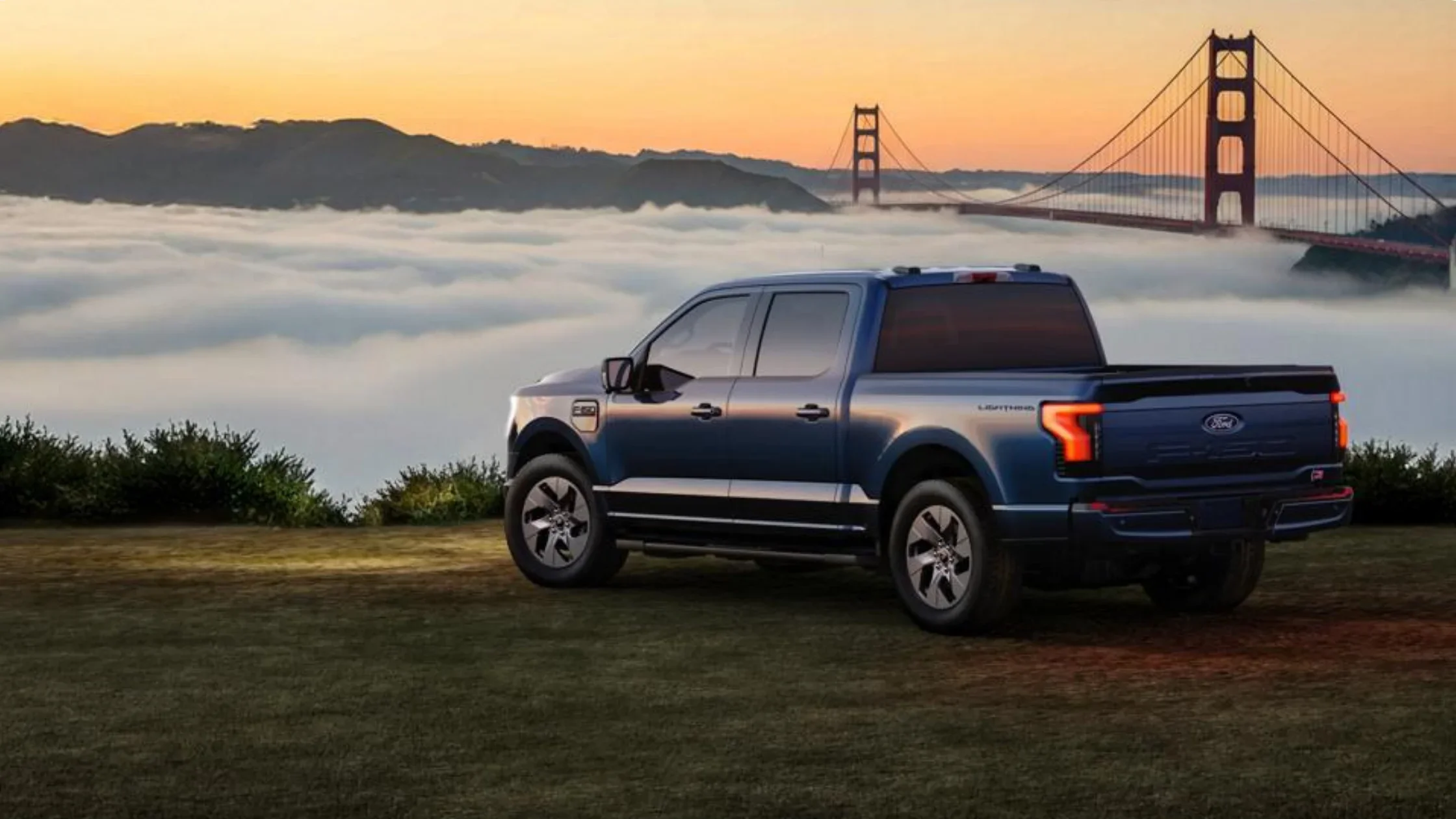 2024 Ford F-150® Lightning in blue parked near Golden Gate Bridge at sunset showing LED taillights and modern truck design