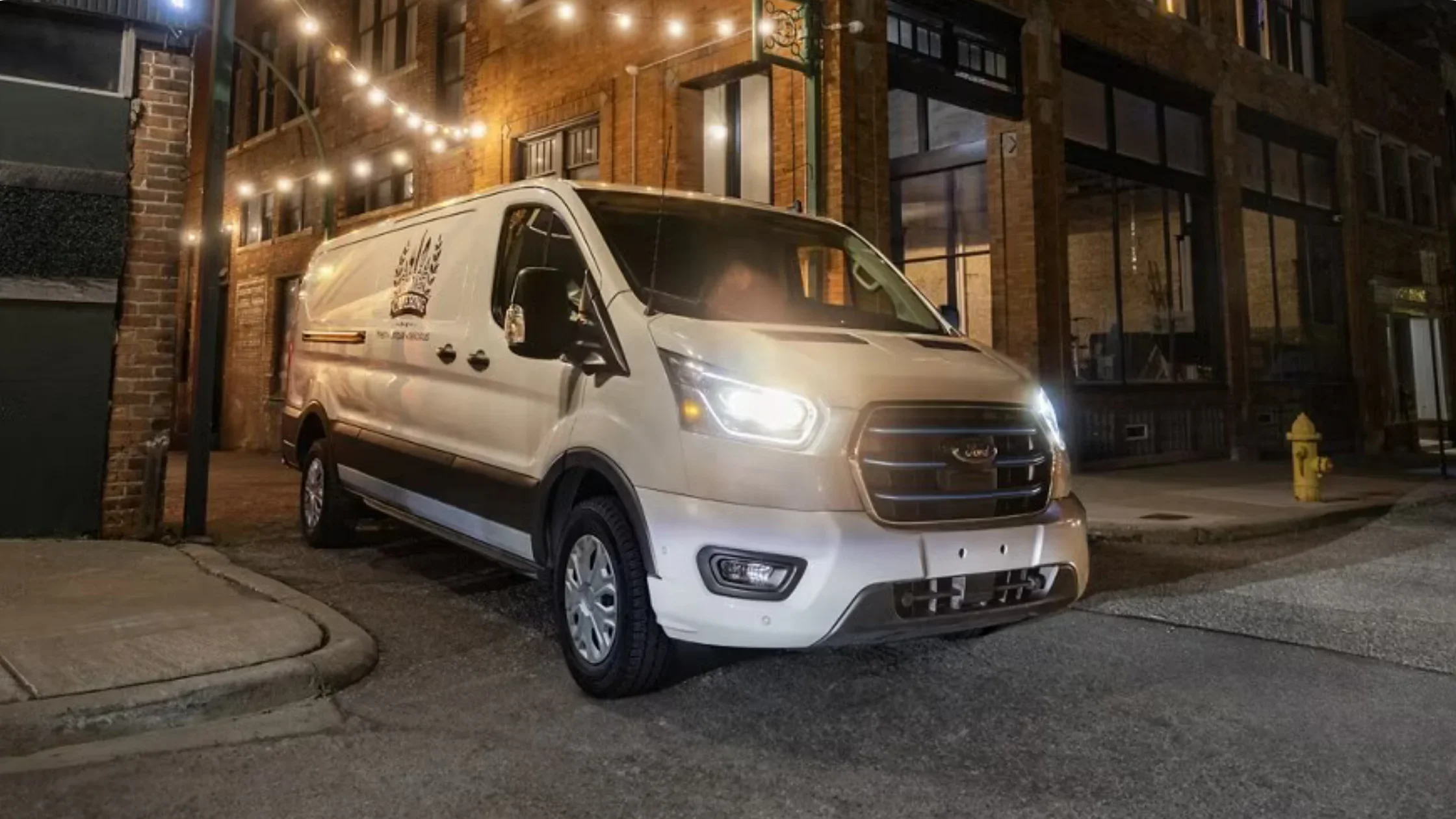 2025 Ford E-Transit™ front view with LED headlights illuminated in an urban street setting at night