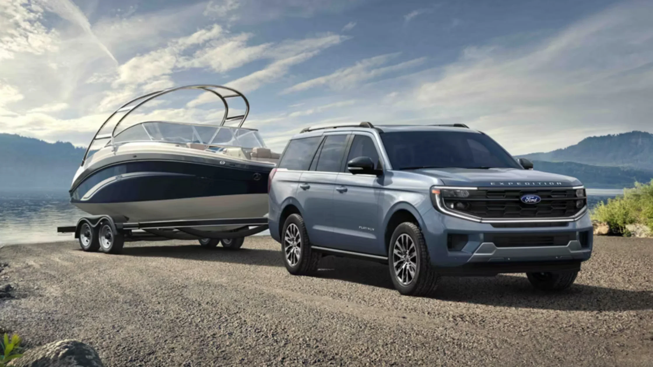 2025 Ford Expedition® towing a luxury boat beside a lake with mountains in the background.