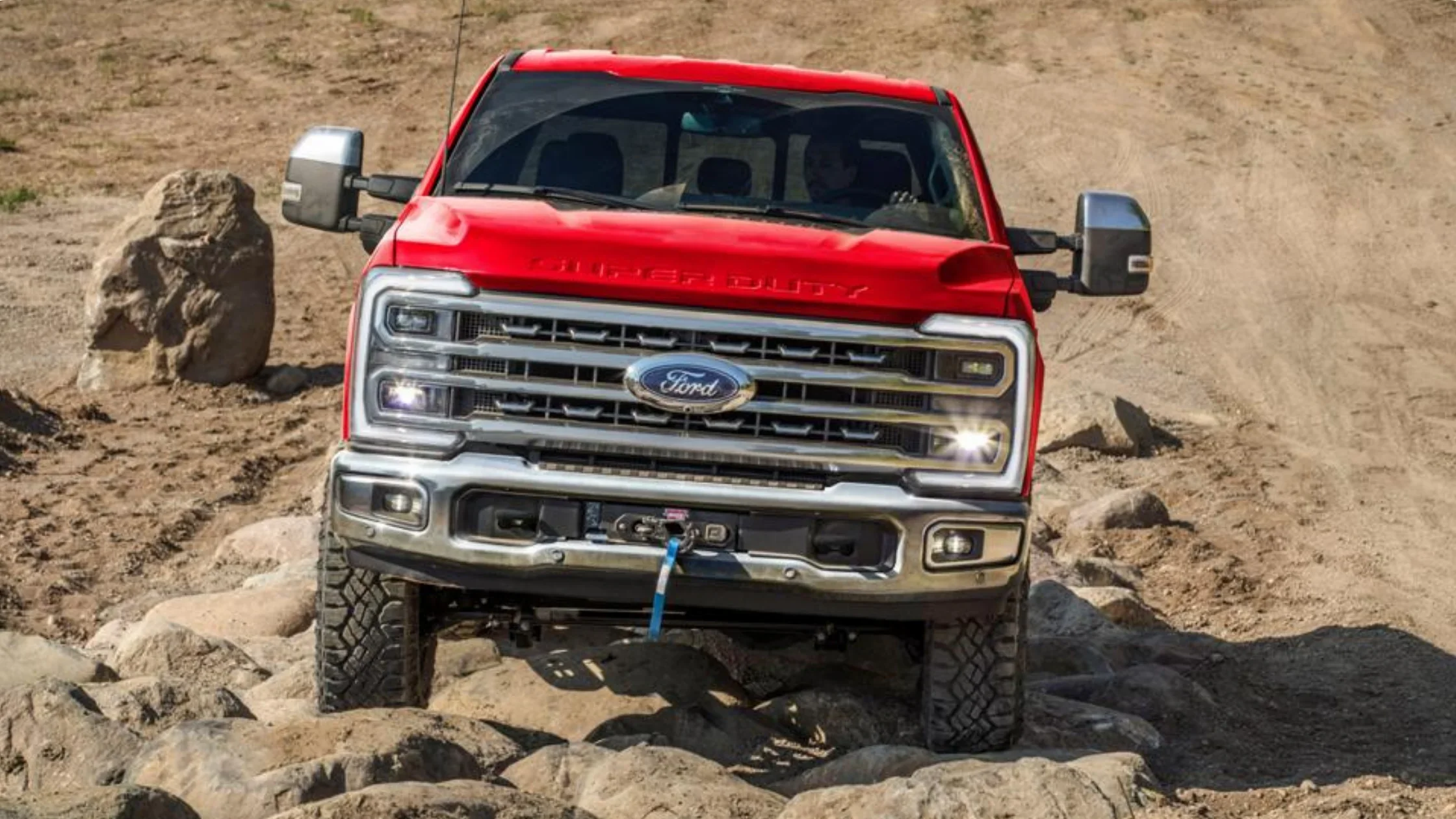Front view of the red 2025 Ford Super Duty® F-250® truck navigating rocky terrain with chrome grille and LED headlights.